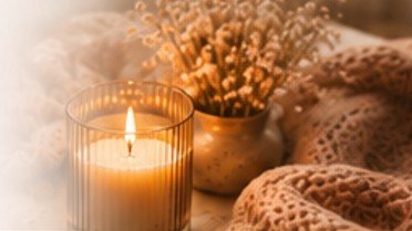 A lit candle beside dried flowers and a soft knit blanket in warm light