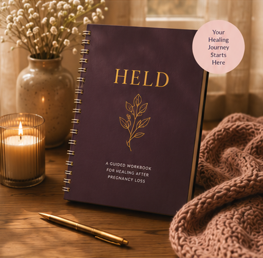 The HELD guided workbook for healing after pregnancy loss, styled with a candle, dried flowers, and a knit blanket, marked with a Your Healing Journey Starts Here badge
